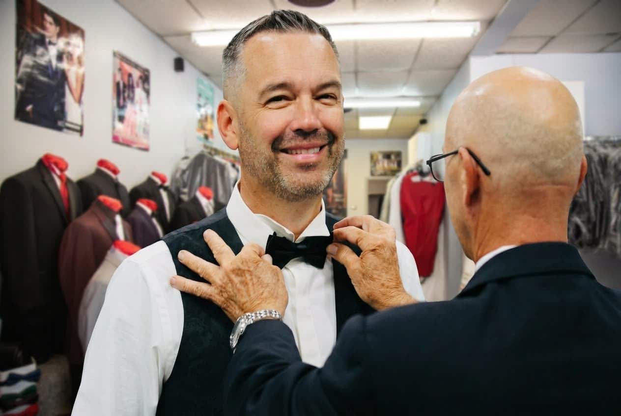 Fitting specialist adjusting a customer's bow tie inside Minsky Formal Wear in Richardson TX